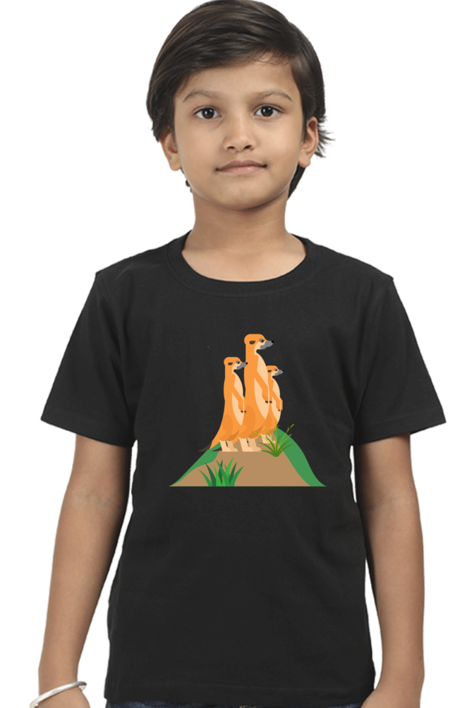 A child wears the MEERKAT Boys T-SHIRT by TuckTribe, showcasing adorable illustrations of three meerkats perched on a grassy mound against a plain white background.