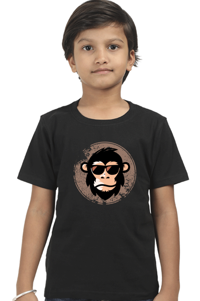 A child with short brown hair confidently wears the TuckTribe COOL CHIMP BOYS T-SHIRT, showcasing a funky chimpanzee in sunglasses centered on a black tee against a circular, textured background, standing against an immaculate white backdrop.