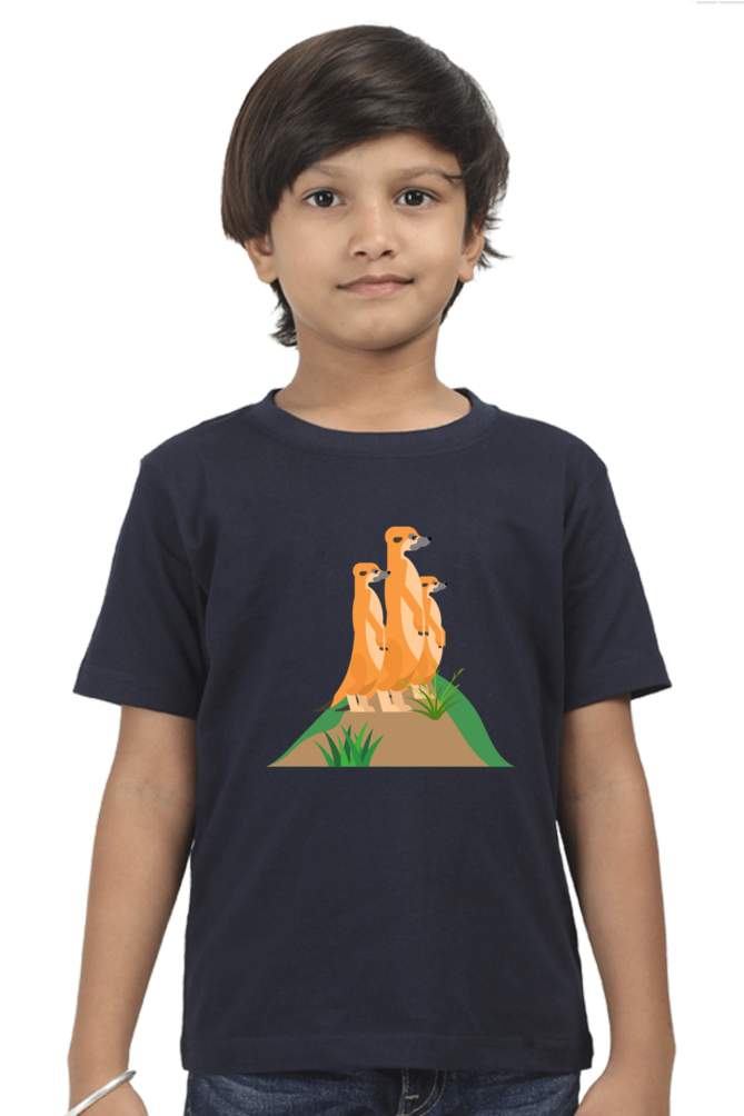 A child with short dark hair wears a TuckTribe MEERKAT boys t-shirt in navy blue, featuring charming illustrations of meerkats standing on a mound.