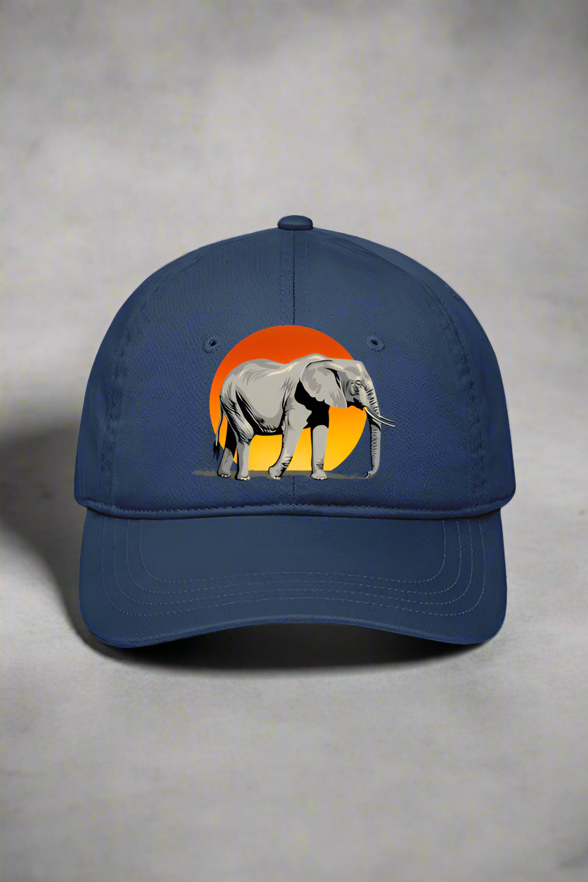 The TuckTribe PRINTED ELEPHANT SPIRIT BASEBALL CAP in blue showcases an embroidered elephant design against an orange sunset circle, capturing natures majesty. It sits on a gray surface with a shadow in the background.