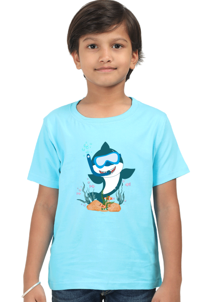 A child models the TuckTribe Smiling Shark Boys T-Shirt, featuring a light blue design of a snorkel-wearing shark above corals. The childs neutral gaze enhances the charm of this aquatic-themed tee.