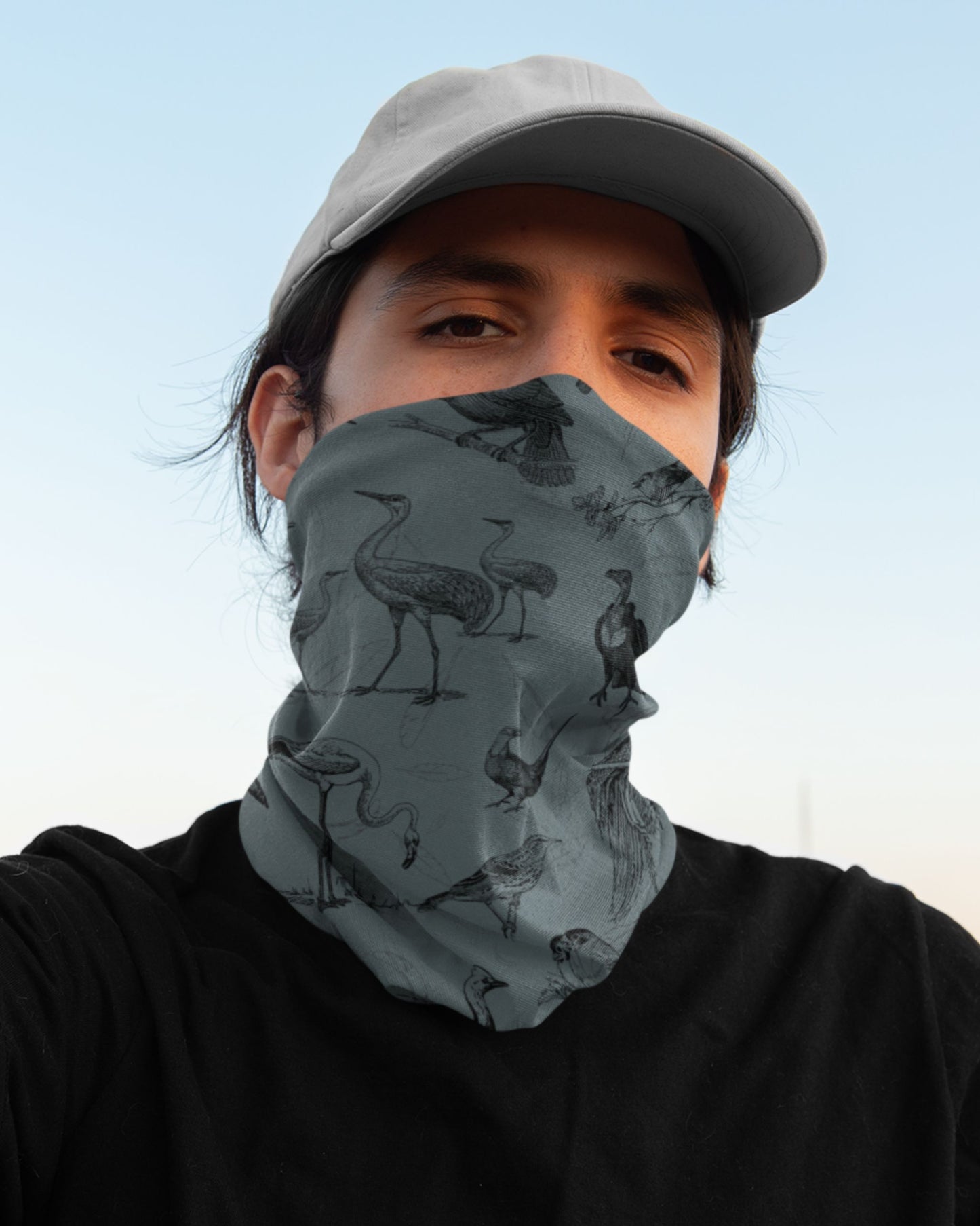 Person wearing a patterned face cover and cap against a clear sky.