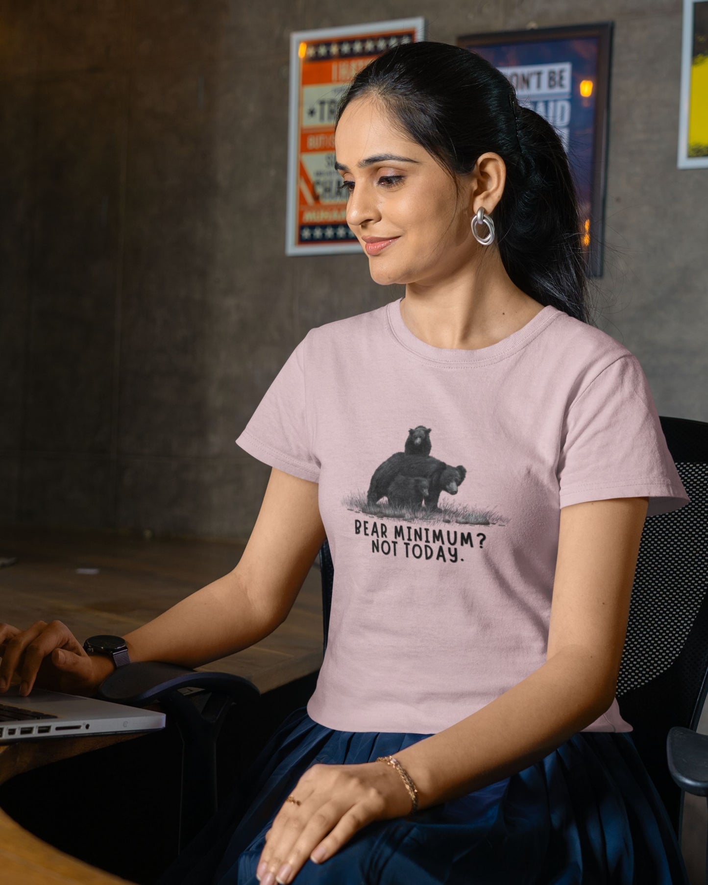 Woman wearing a pink t-shirt with a bear graphic and text, sitting in an office setting.