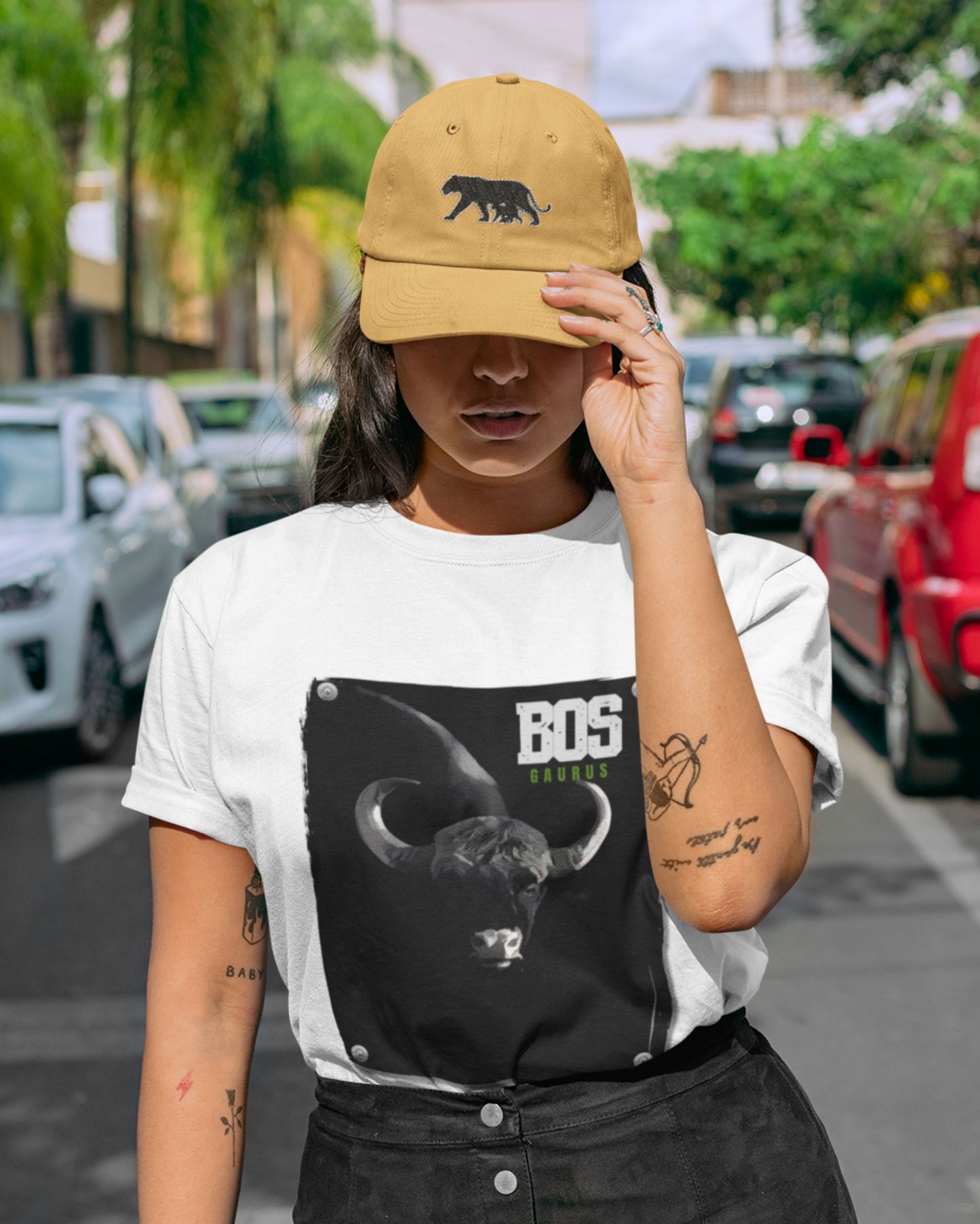 Person wearing a white t-shirt with a black graphic design and a yellow cap in an urban setting.