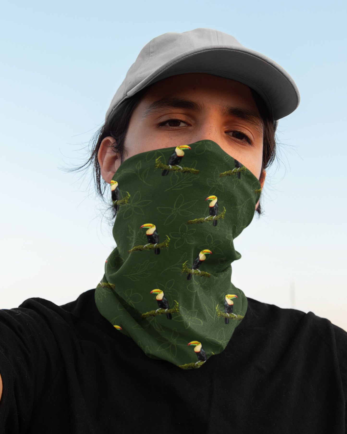 Person wearing a green tucktribe neck gaiter with toucan designs against a clear blue sky.