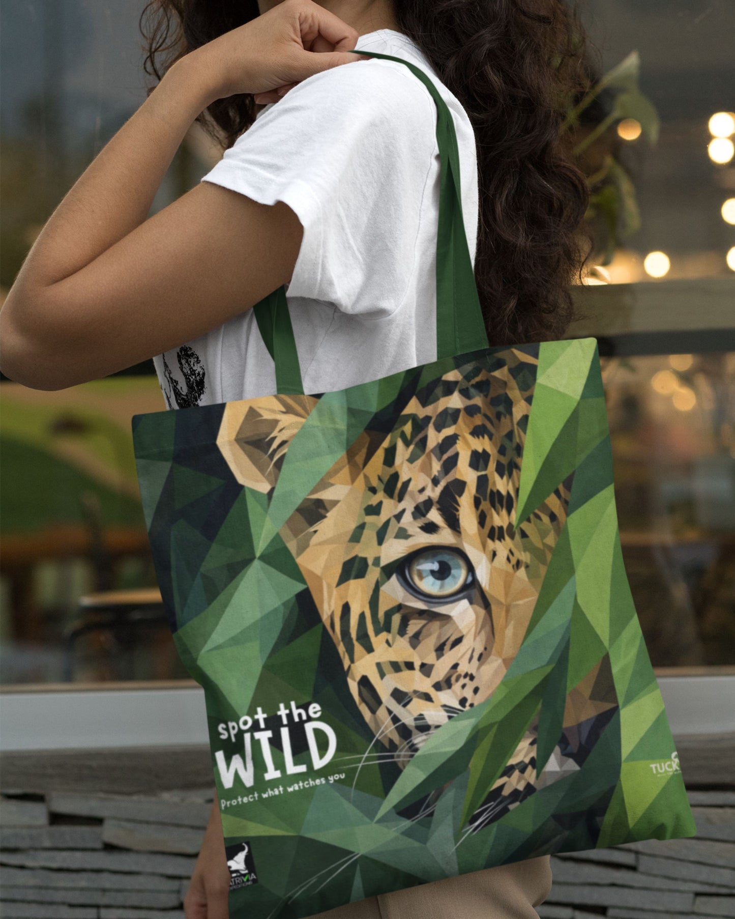 Person holding a tucktribe tote bag with a leopard design and 'spot the wild' text.