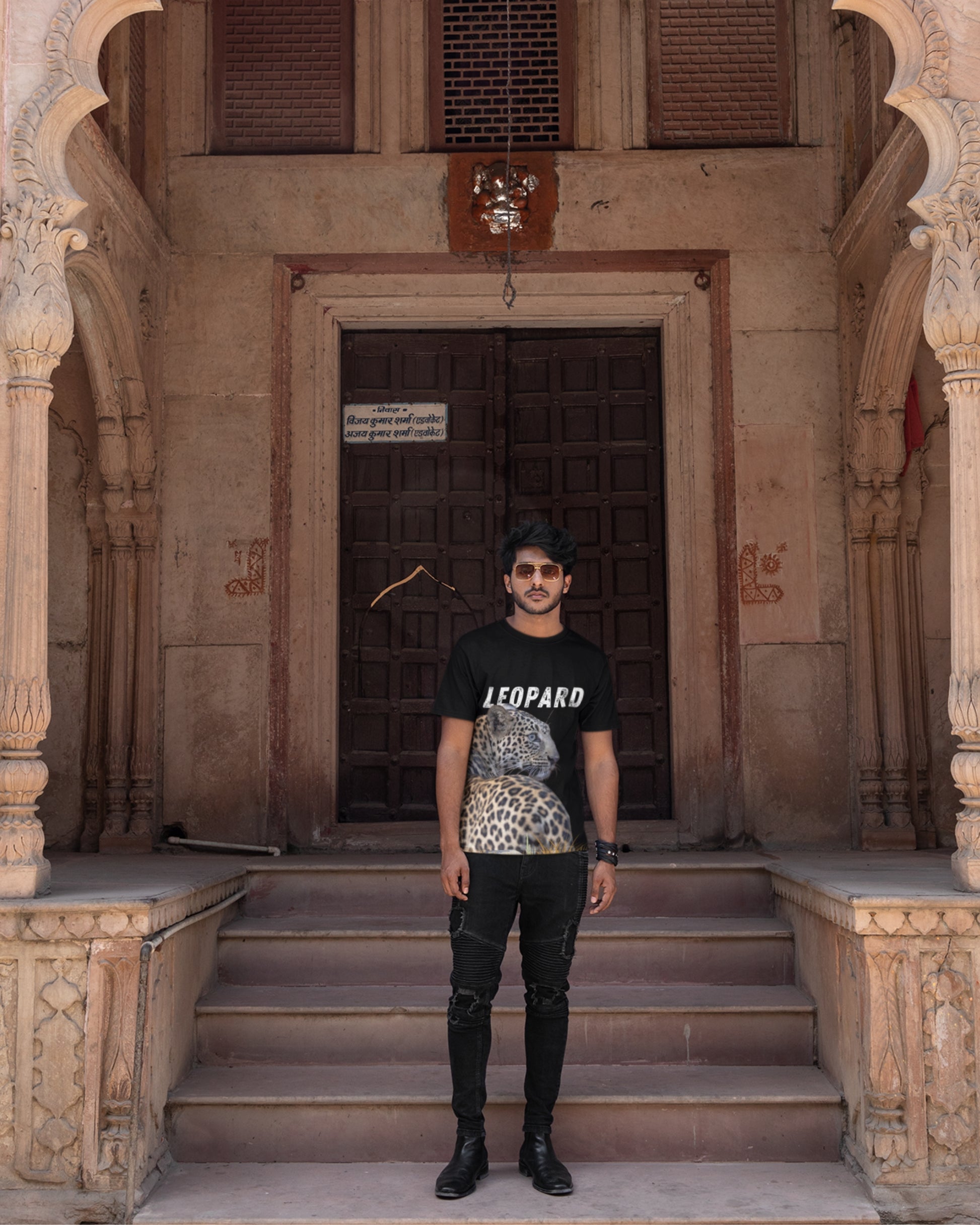 A man standing in front of a old building wearing a tshirt with leopard graphics and text LEOPARD