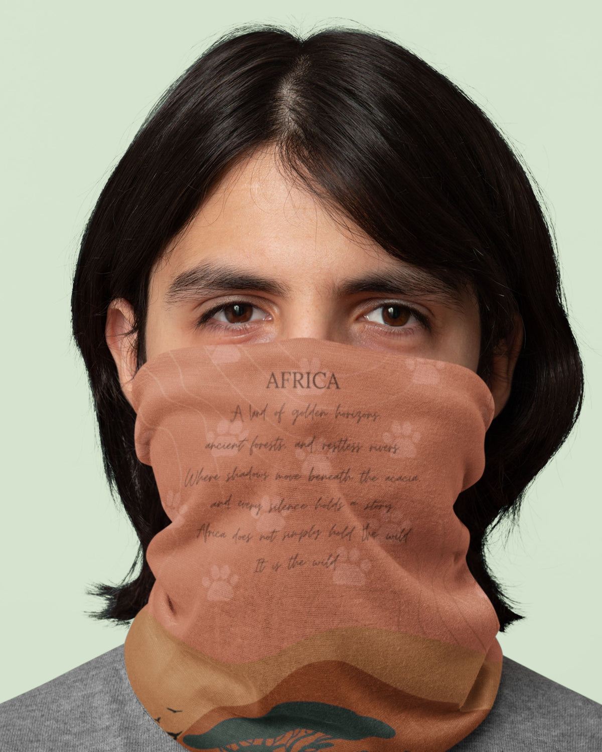 A person wearing a terracotta-colored face covering or neck gaiter with a printed 'AFRICA' landscape design, shown against a solid pale green background.