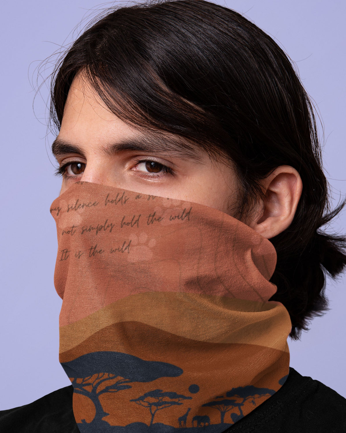 A person wearing a terracotta orange and brown neck gaiter with a printed landscape design of acacia trees and elephants, and cursive text, against a solid lavender background.