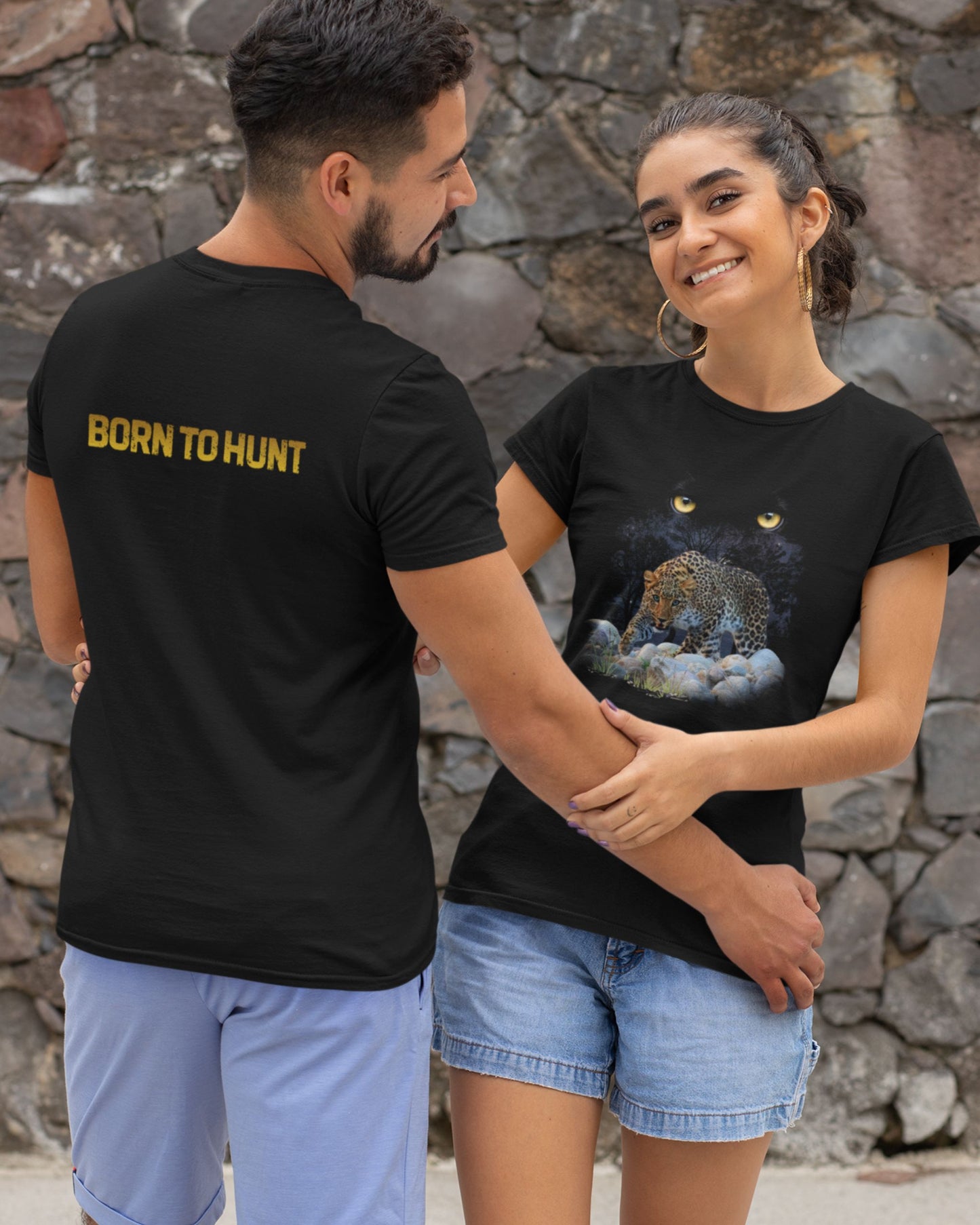 Two people wearing black tucktribe t-shirts with a leopard graphic and 'Born to Hunt' text, standing against a stone wall.