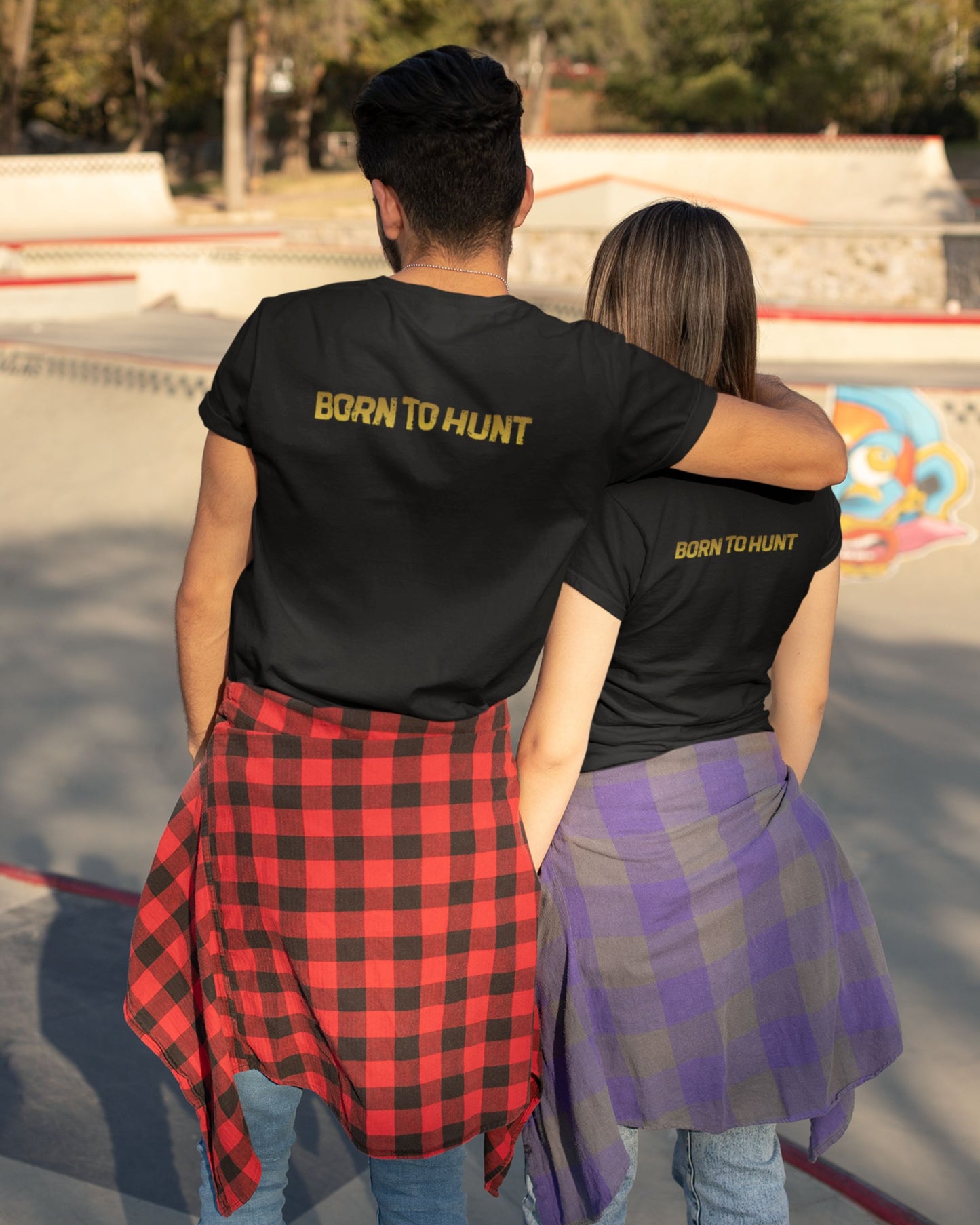 Two people wearing black tucktribe t-shirts with 'BORN TO HUNT' text, standing in a skate park.