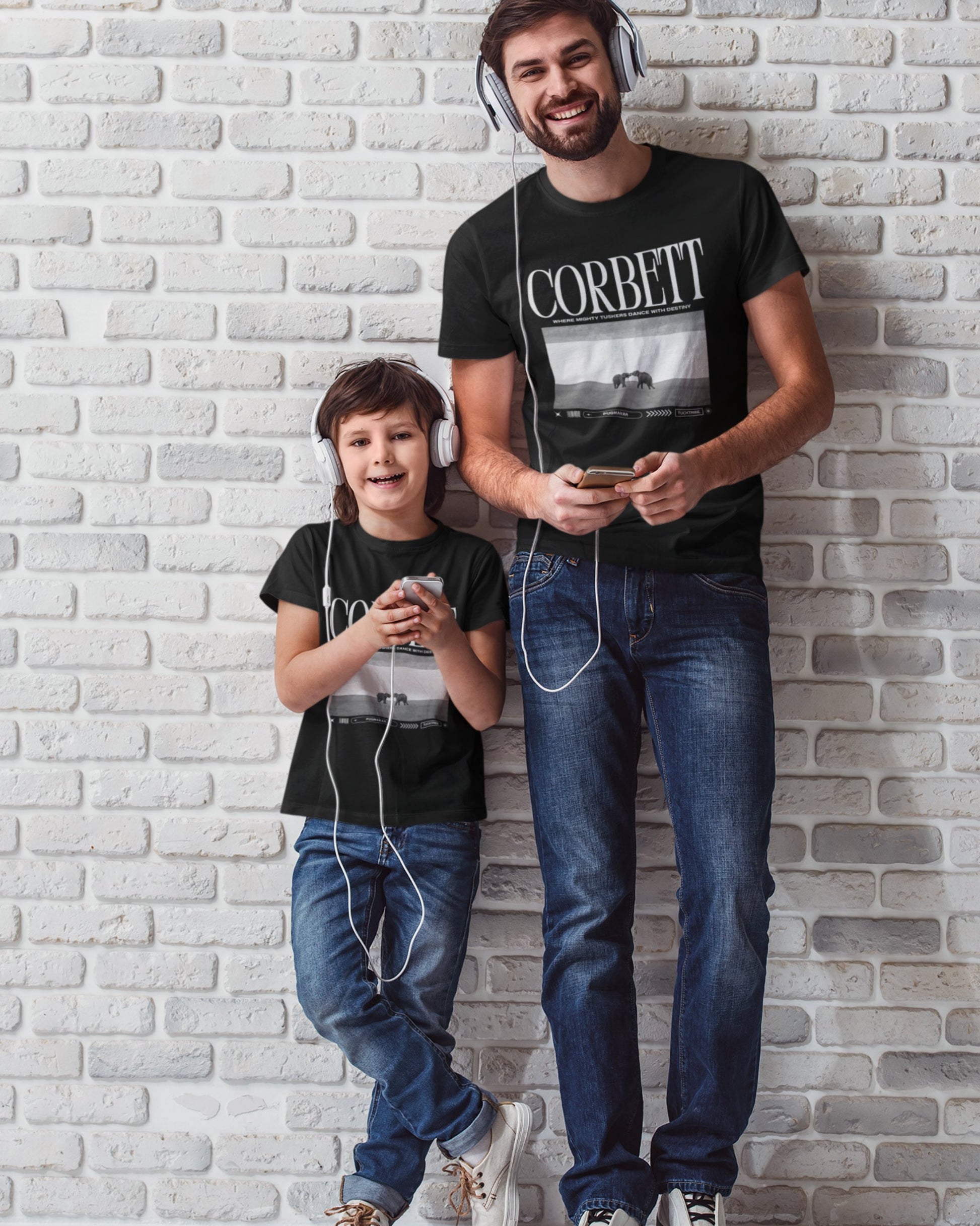 Man and child standing against a brick wall, both wearing headphones and using devices.