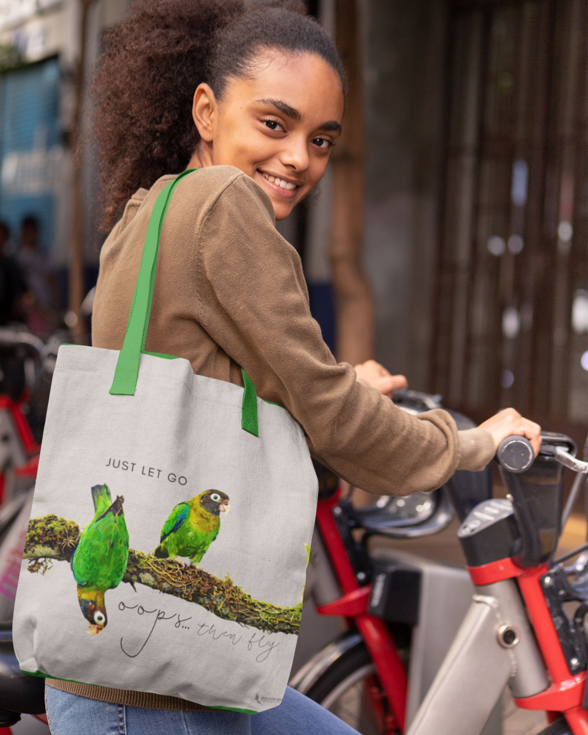 Woman holding a Tucktribe tote bag with Brown headed parrot design and text outdoors
