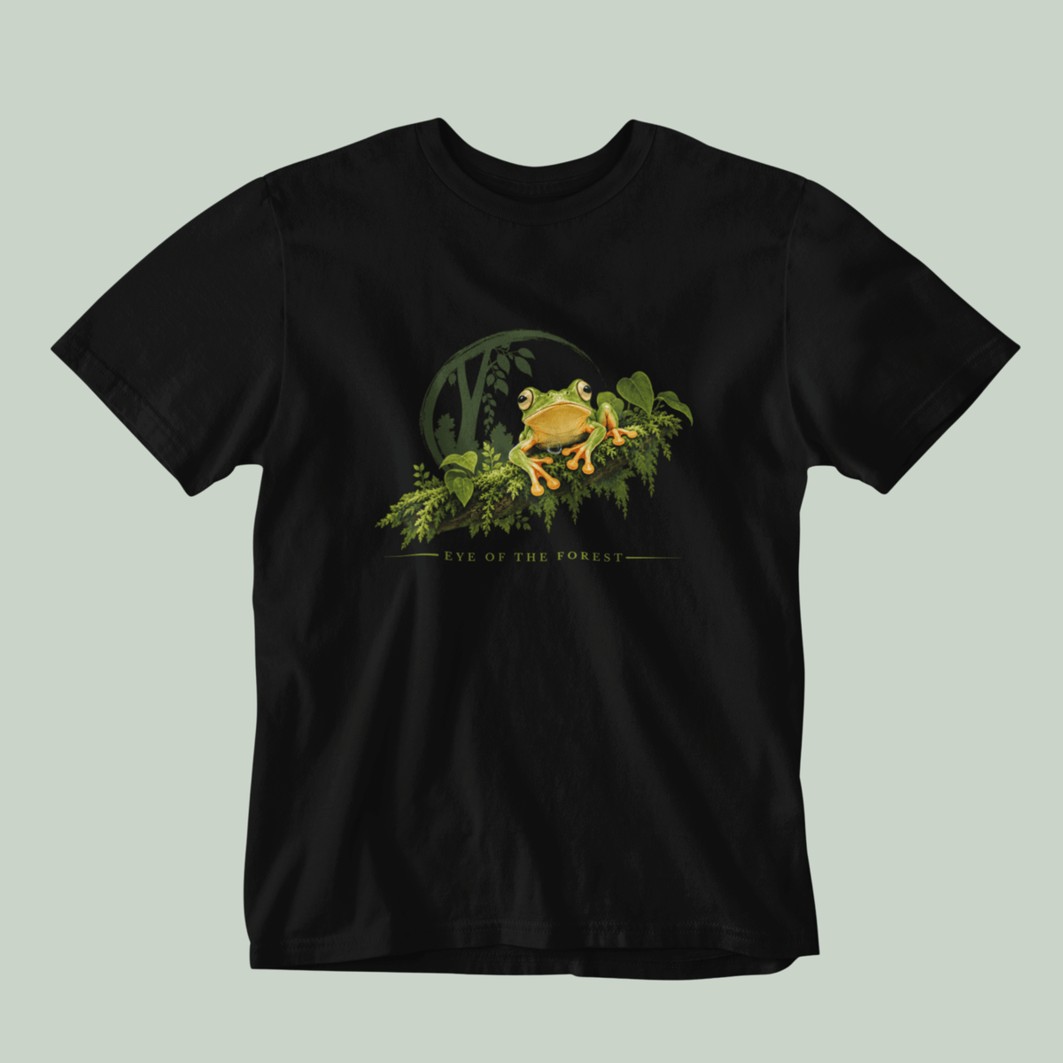 A black short-sleeve crewneck t-shirt featuring a graphic print of a malabar gliding frog sitting on a branch with the text 'EYE OF THE FOREST' underneath, displayed against a solid light sage green background.