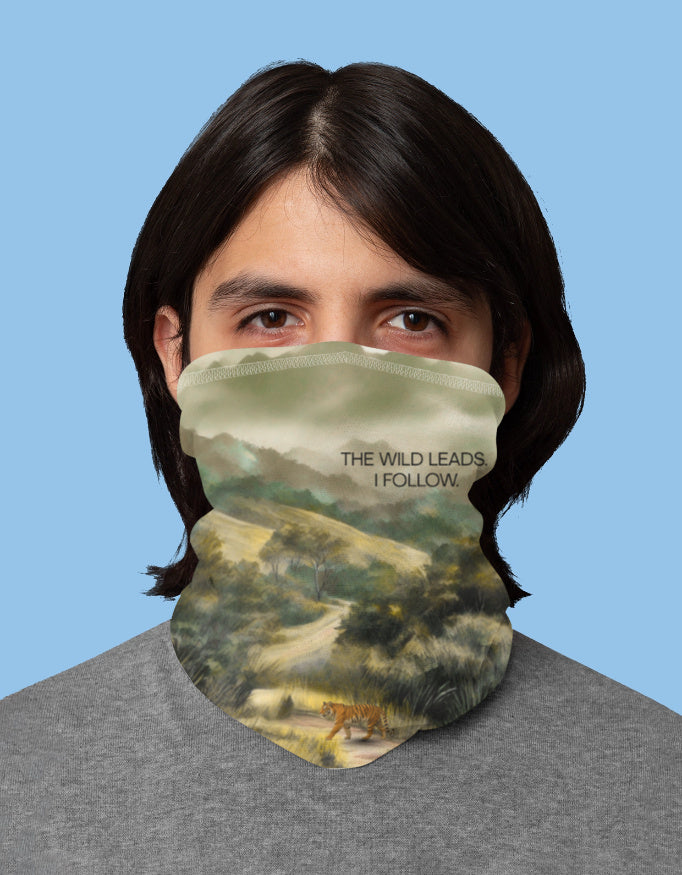 Person wearing a neck gaiter with a scenic design and text against a blue background