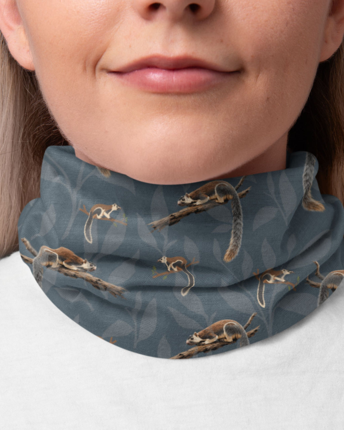 Close-up of a person wearing a grayish-blue neck gaiter with a repeating print of grizzled giant squirrel  on branches.
