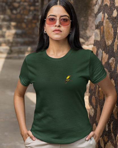 Woman wearing a Tucktribe green t-shirt with a embroidery of a golden oriole bird against a stone wall background