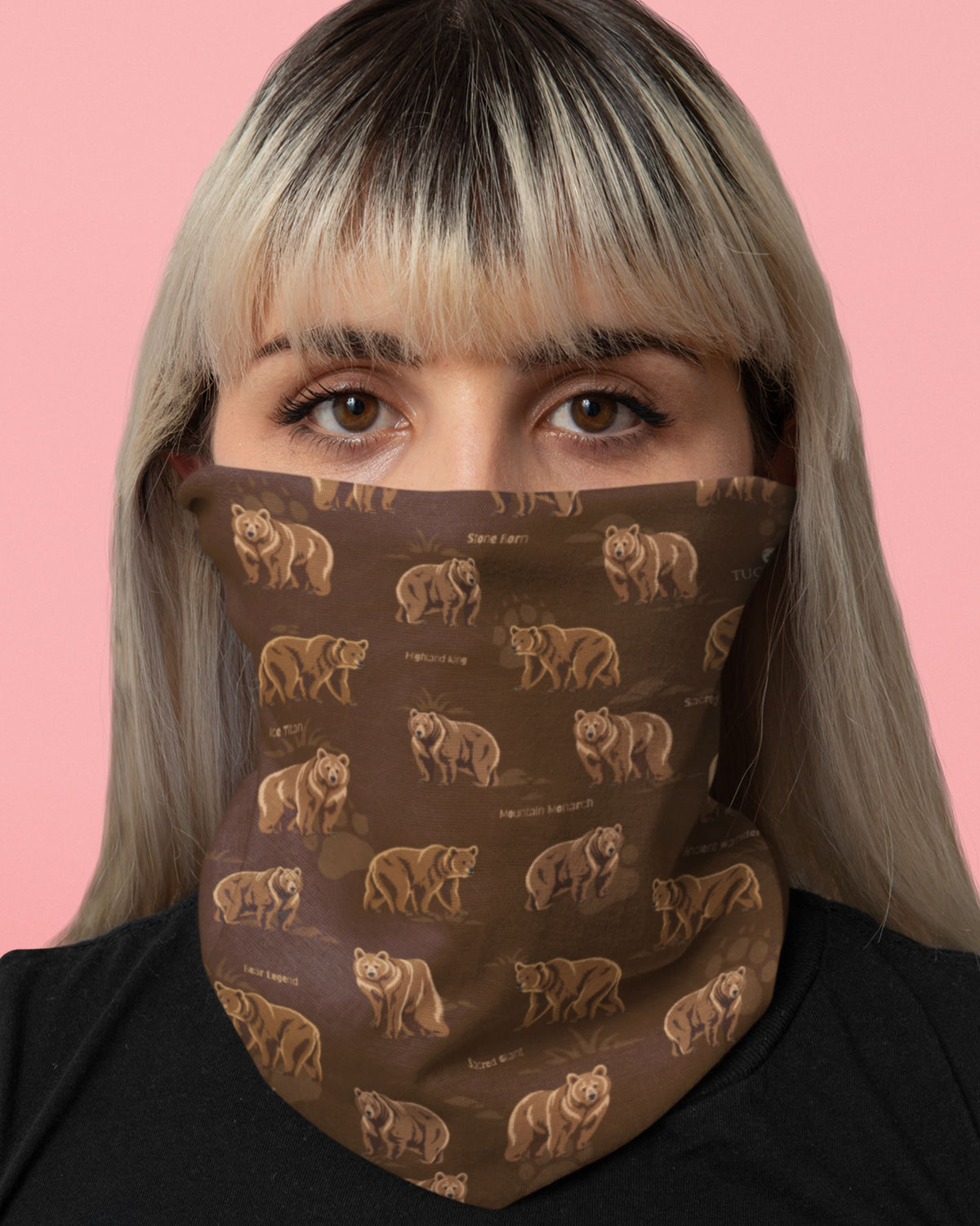 A close-up of a person wearing a brown neck gaiter or face mask with an allover print of Himalayan brown bears, set against a solid pink background.