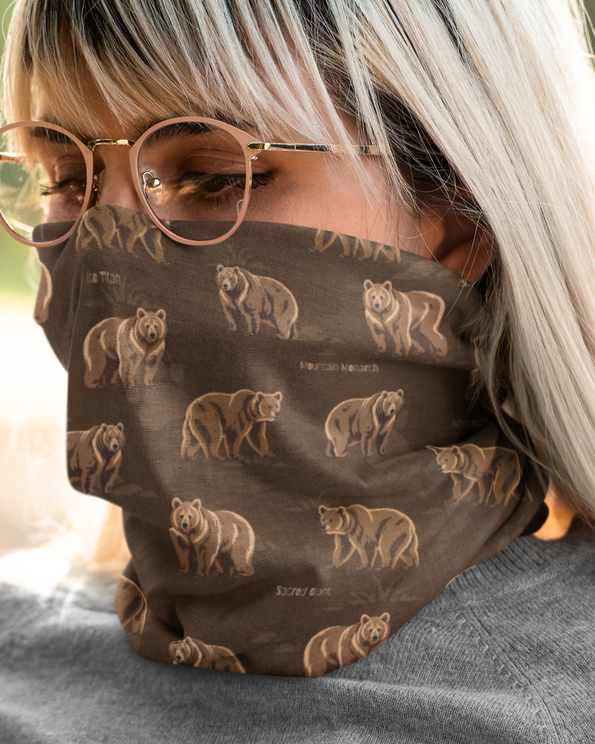 A close-up of a person wearing a brown face mask with a repeating print of Himalayan bears and small text, along with round eyeglasses and a gray top.