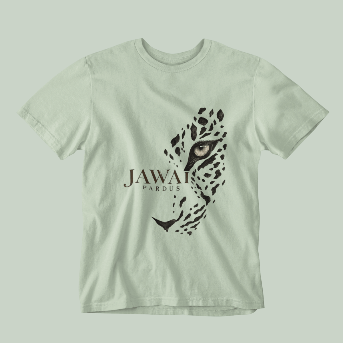 A light sage green short-sleeve t-shirt featuring a graphic print of a leopard's face and the text 'JAWAI PARDUS' on the front, displayed against a matching light sage green background.