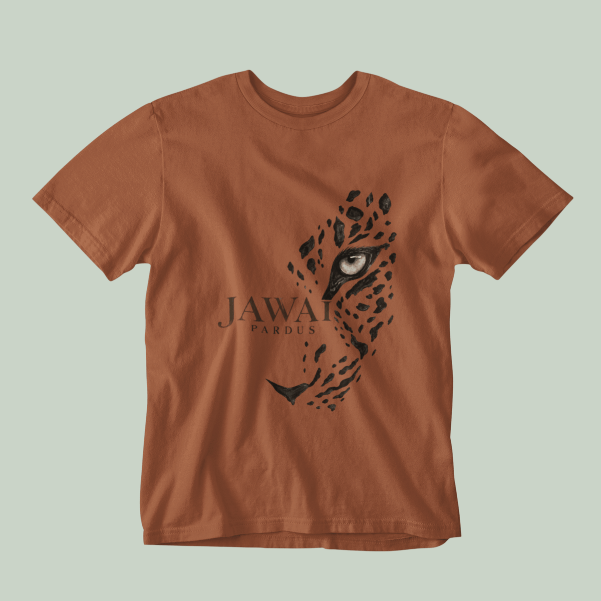 A copper short-sleeve crewneck t-shirt featuring a black graphic of a leopard face and the text 'JAWAI PARDUS' printed on the front, set against a solid pale sage green background.