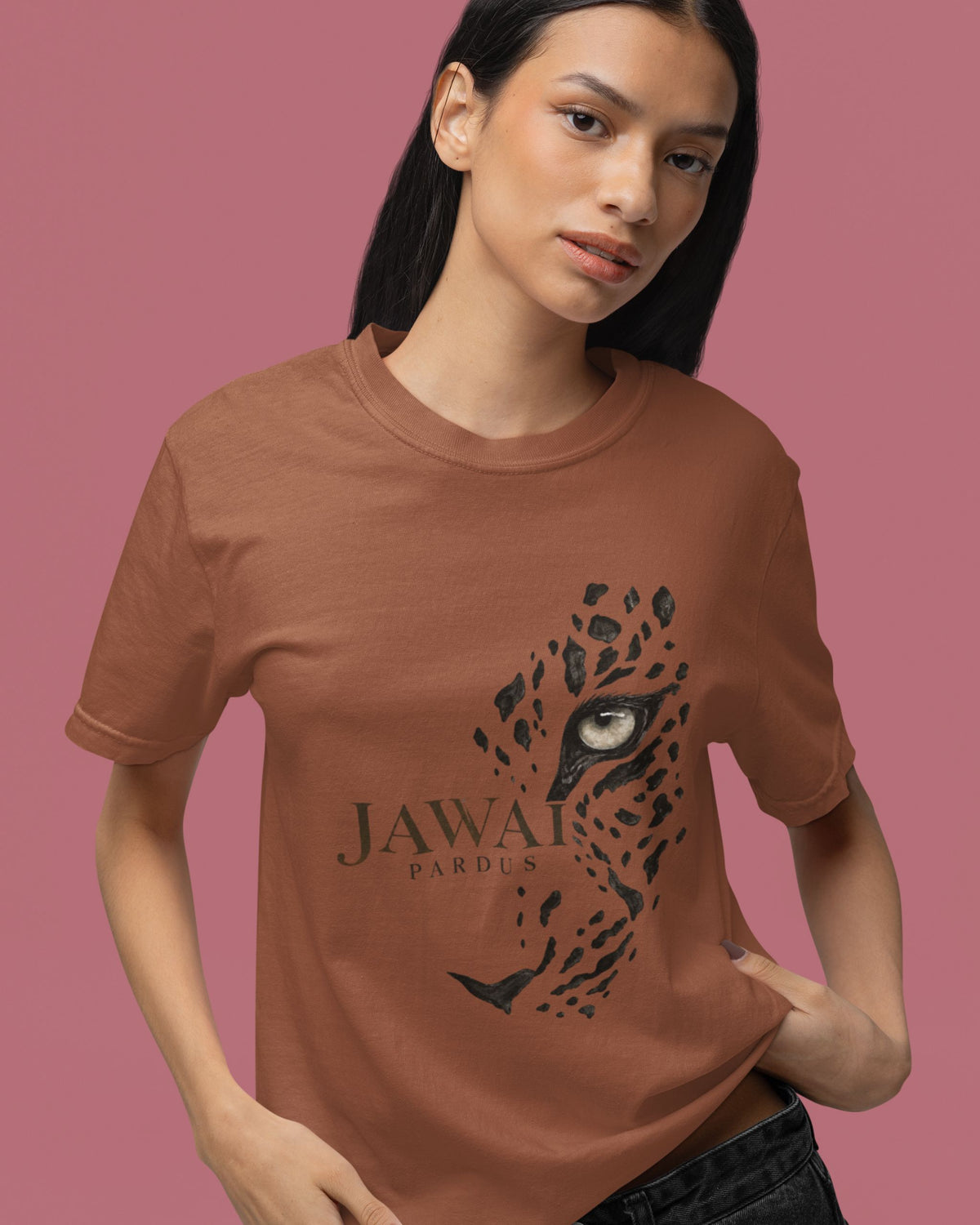 A woman modeling a copper brown short-sleeve t-shirt with a black graphic of a leopard face and the text 'JAWAI PARDUS' on the front, set against a solid dusty pink background.