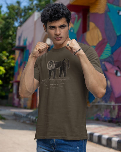 A man wearing an olive green t-shirt with a black graphic of a Lion tailed macaque on the front, posing in front of a colorful graffiti wall.