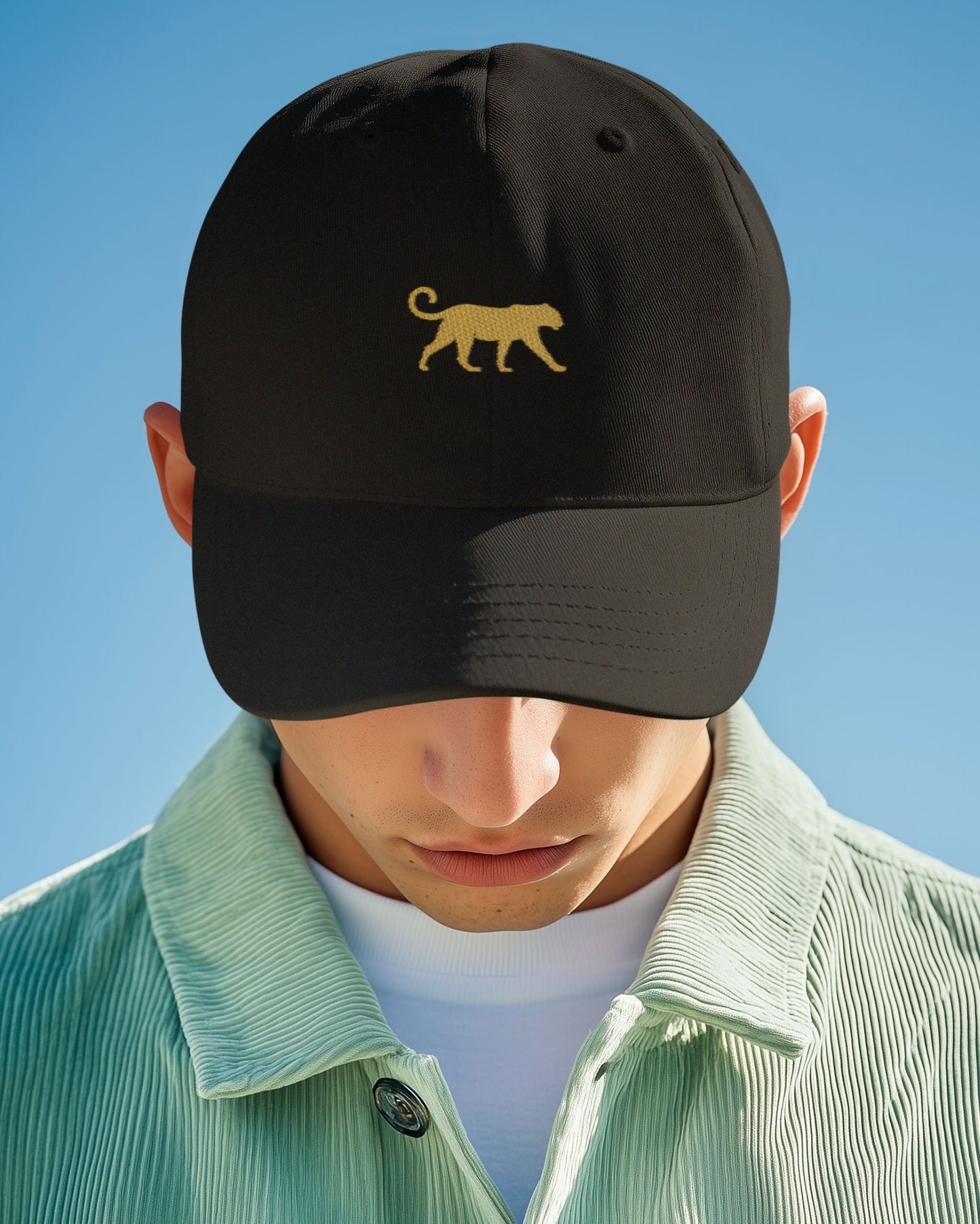 Person wearing a Tucktribe black cap with a gold panther logo against a clear blue sky
