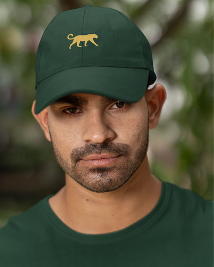Man wearing a tucktribe bottle green cap with a yellow panther logo against a blurred natural background