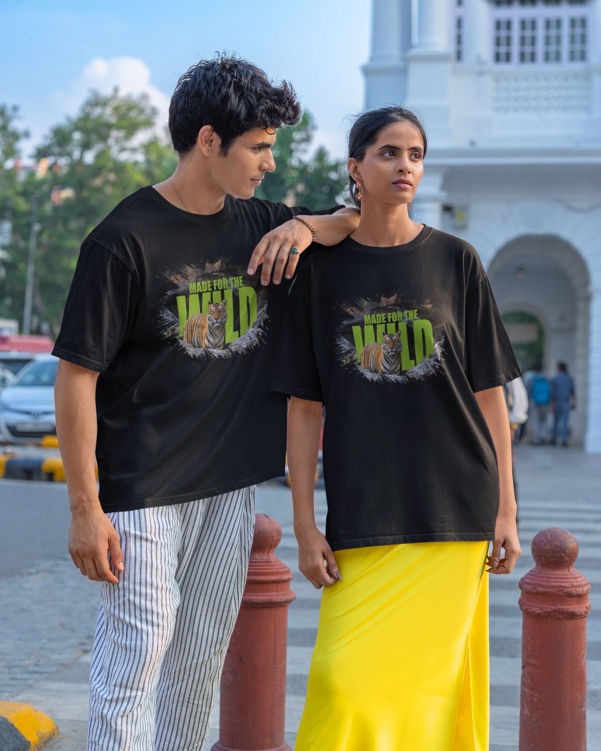 Two people wearing matching black t-shirts with a graphic design in an outdoor setting.