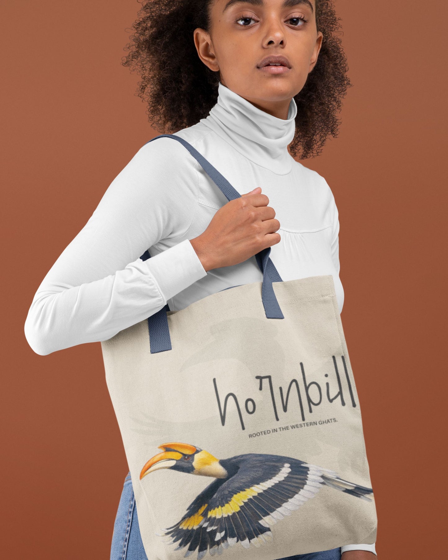 Person holding a tucktribe tote bag with a hornbill design and text on a brown background