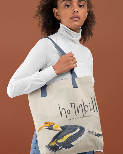 Person holding a tucktribe tote bag with a hornbill design and text on a brown background