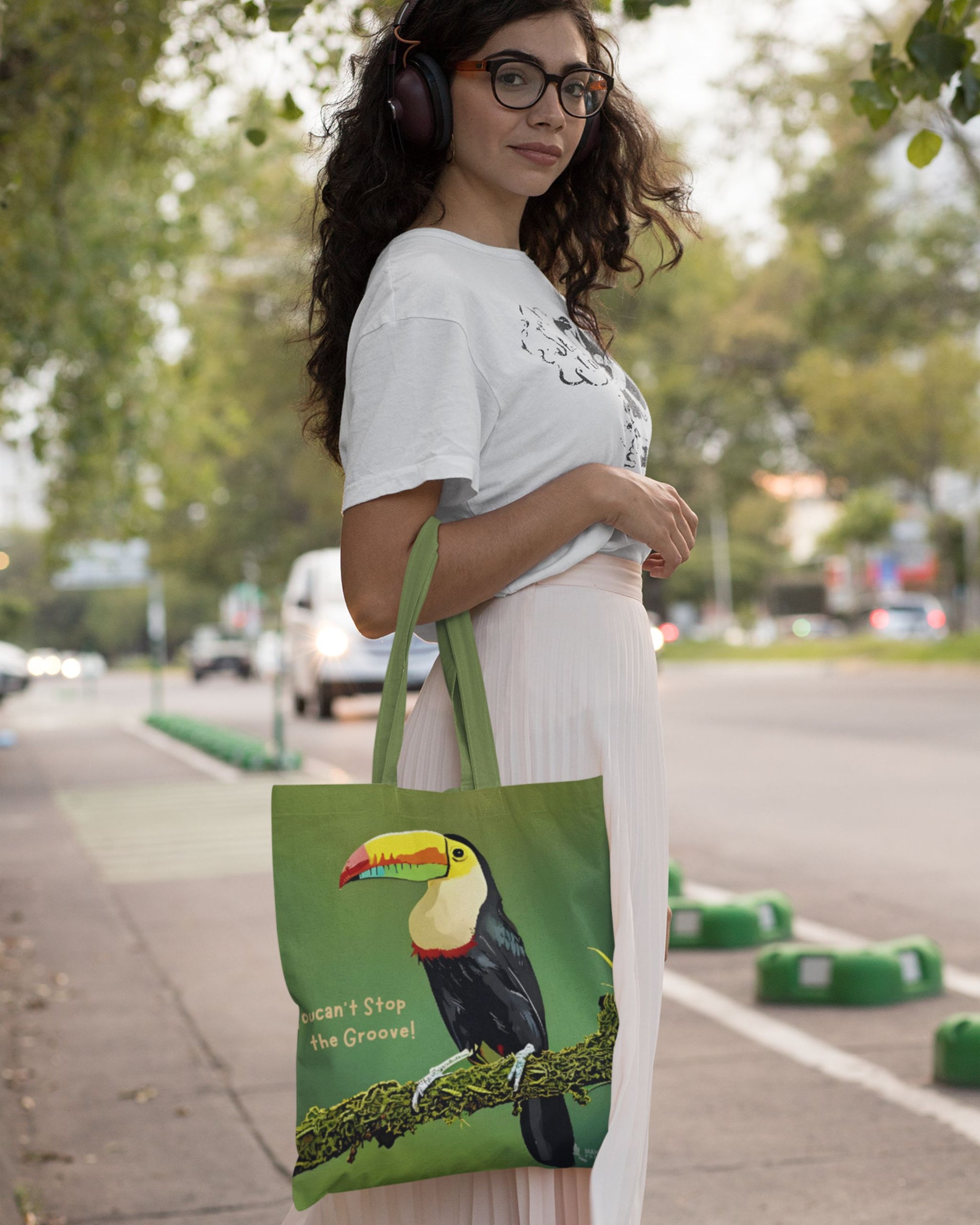 Woman holding a green tucktribe tote bag with a toucan design outdoors.