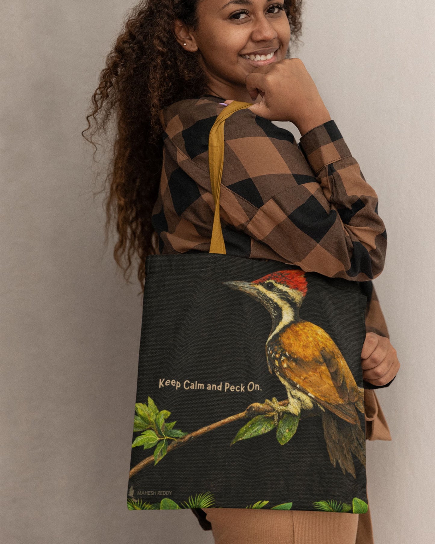 Person holding a tucktribe tote bag with a woodpecker design and text.