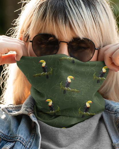 Person wearing a green tucktribe face buff with toucan patterns, sunglasses, and denim jacket.
