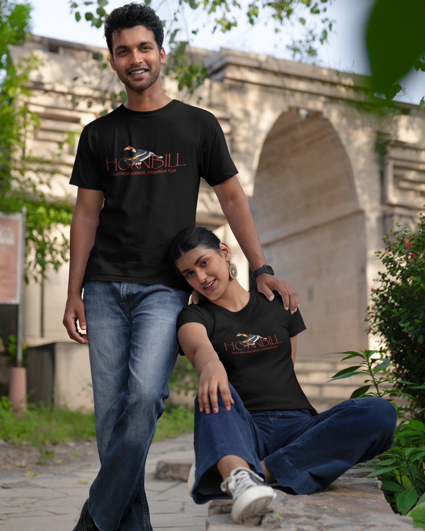 Two people wearing black tucktribe t-shirts with a hornbill design in front of a stone archway.