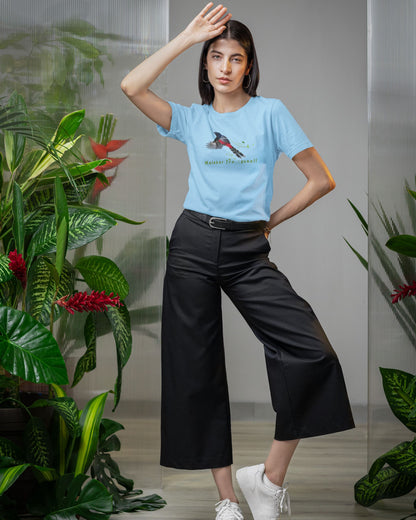 Woman wearing a light blue t-shirt with a graphic design, standing among plants.