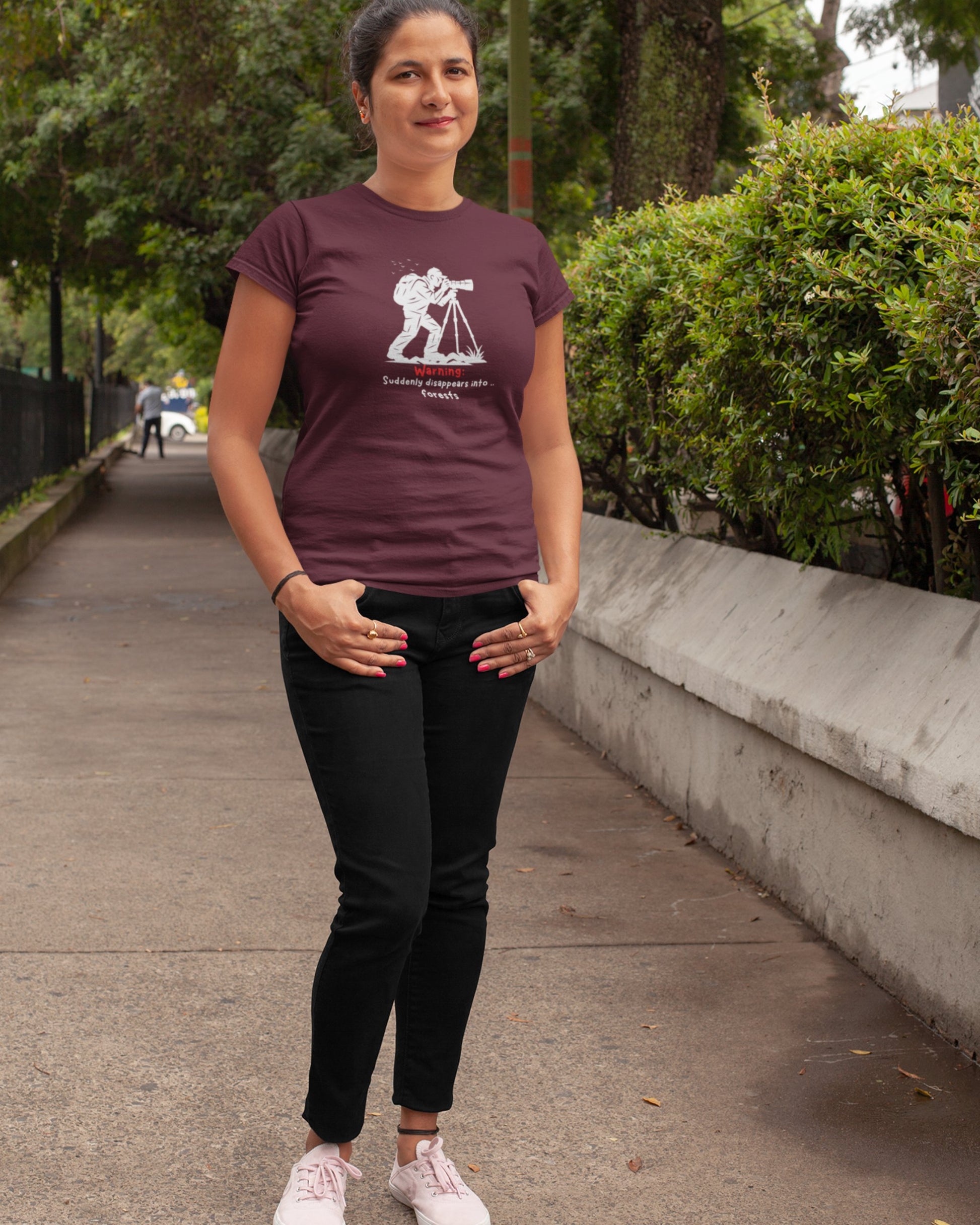 Woman wearing a maroon t-shirt with a graphic design, standing outdoors on a sidewalk.