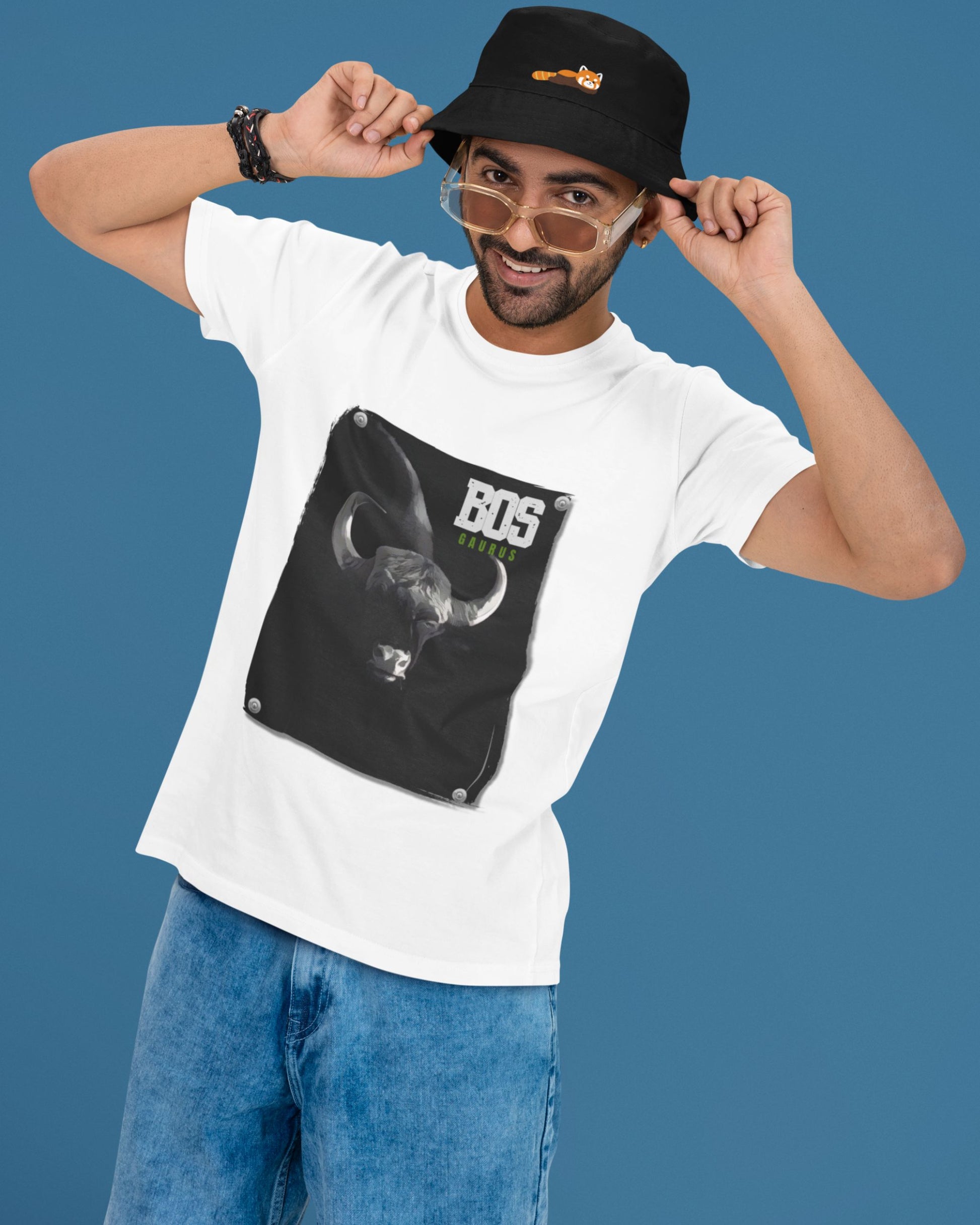 Man wearing a white t-shirt with a graphic design and text, blue pants, and a black cap on a blue background