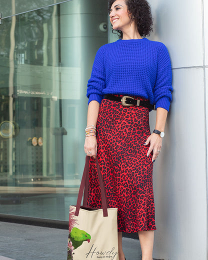 Woman wearing a blue sweater and red leopard print skirt, holding a Tucktribe tote bag with a Hanging parrot design.