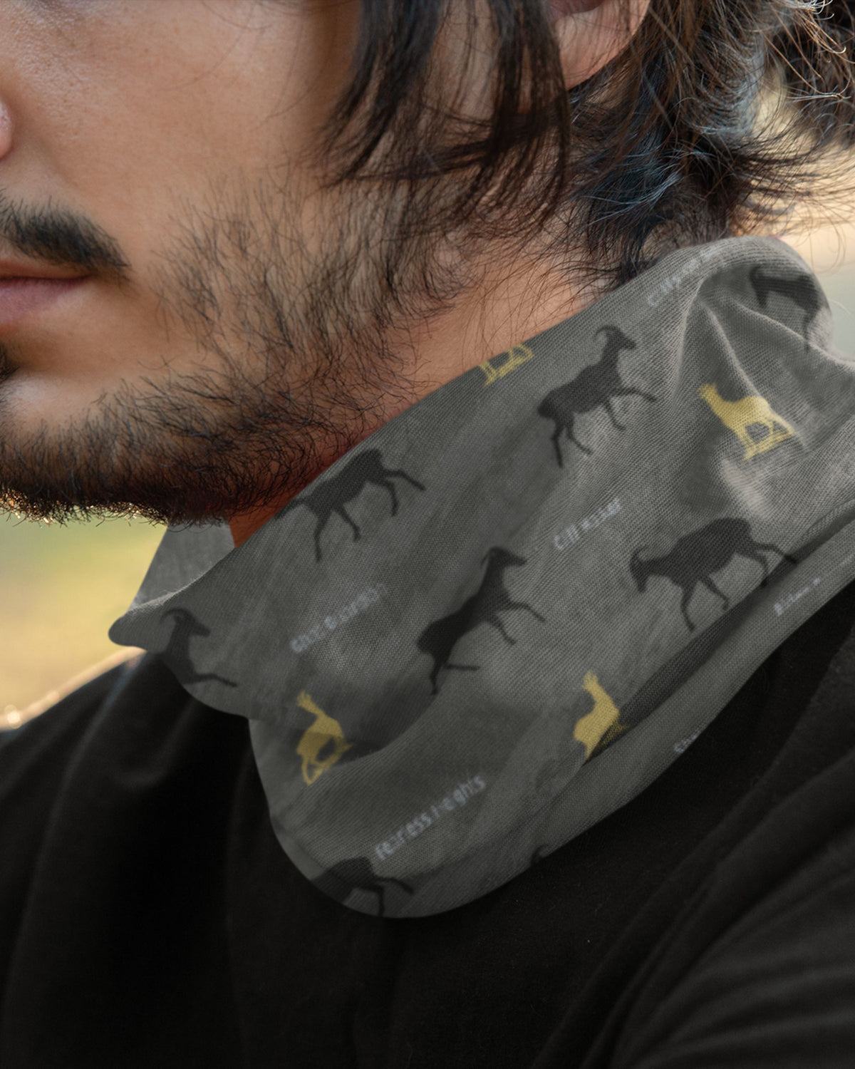 A close-up of a man wearing a gray neck gaiter with a pattern of black and yellow Nilgiri Thar and few texts printed in white.