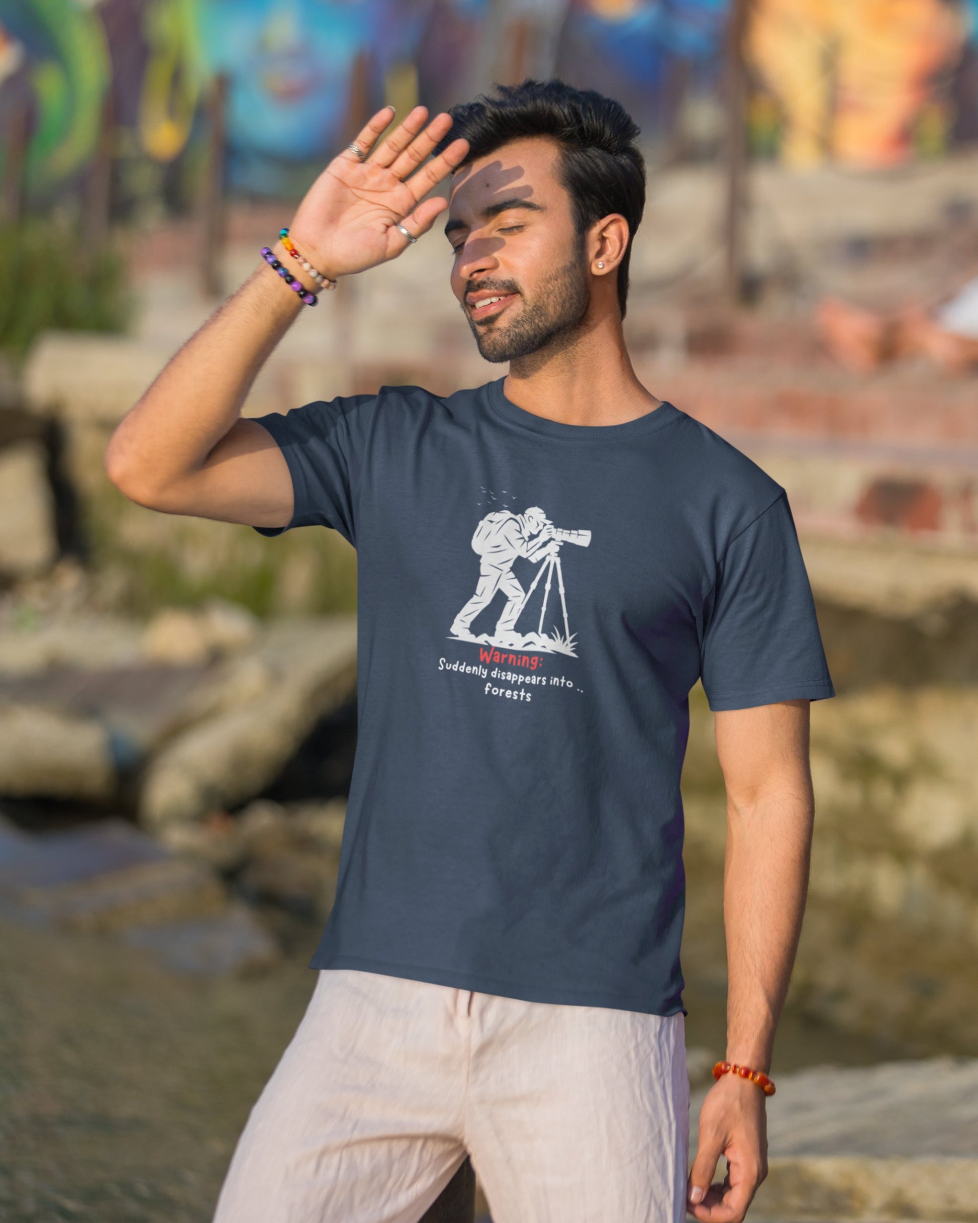 Man wearing a navy blue t-shirt with a graphic design, standing outdoors near water.