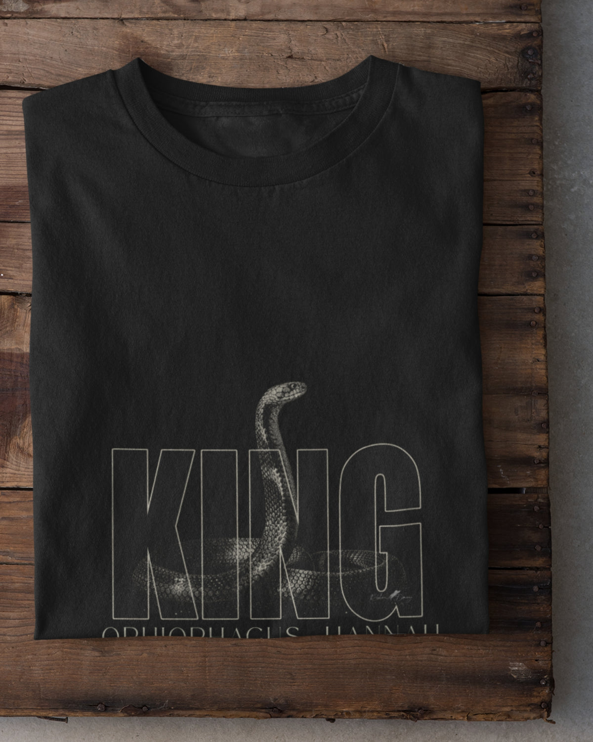 King Cobra wildlife T-shirt featuring detailed Ophiophagus hannah snake artwork with bold KING typography placed on a wooden plank.