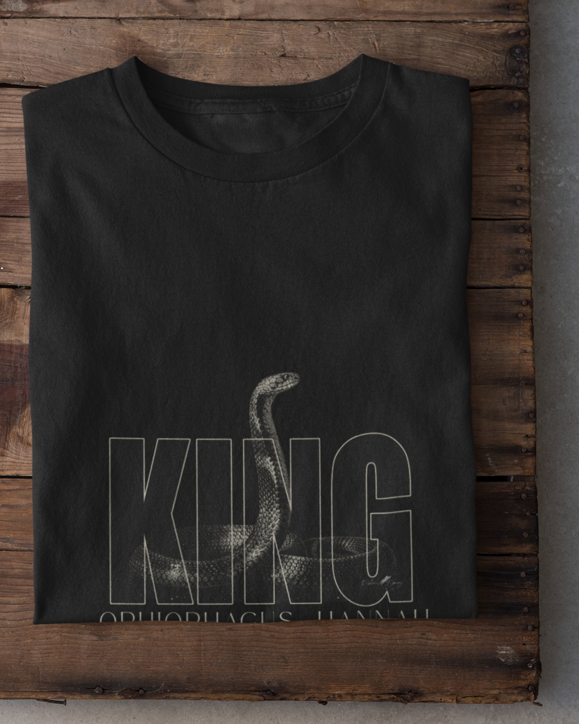 King Cobra wildlife T-shirt featuring detailed Ophiophagus hannah snake artwork with bold KING typography placed on a wooden plank.