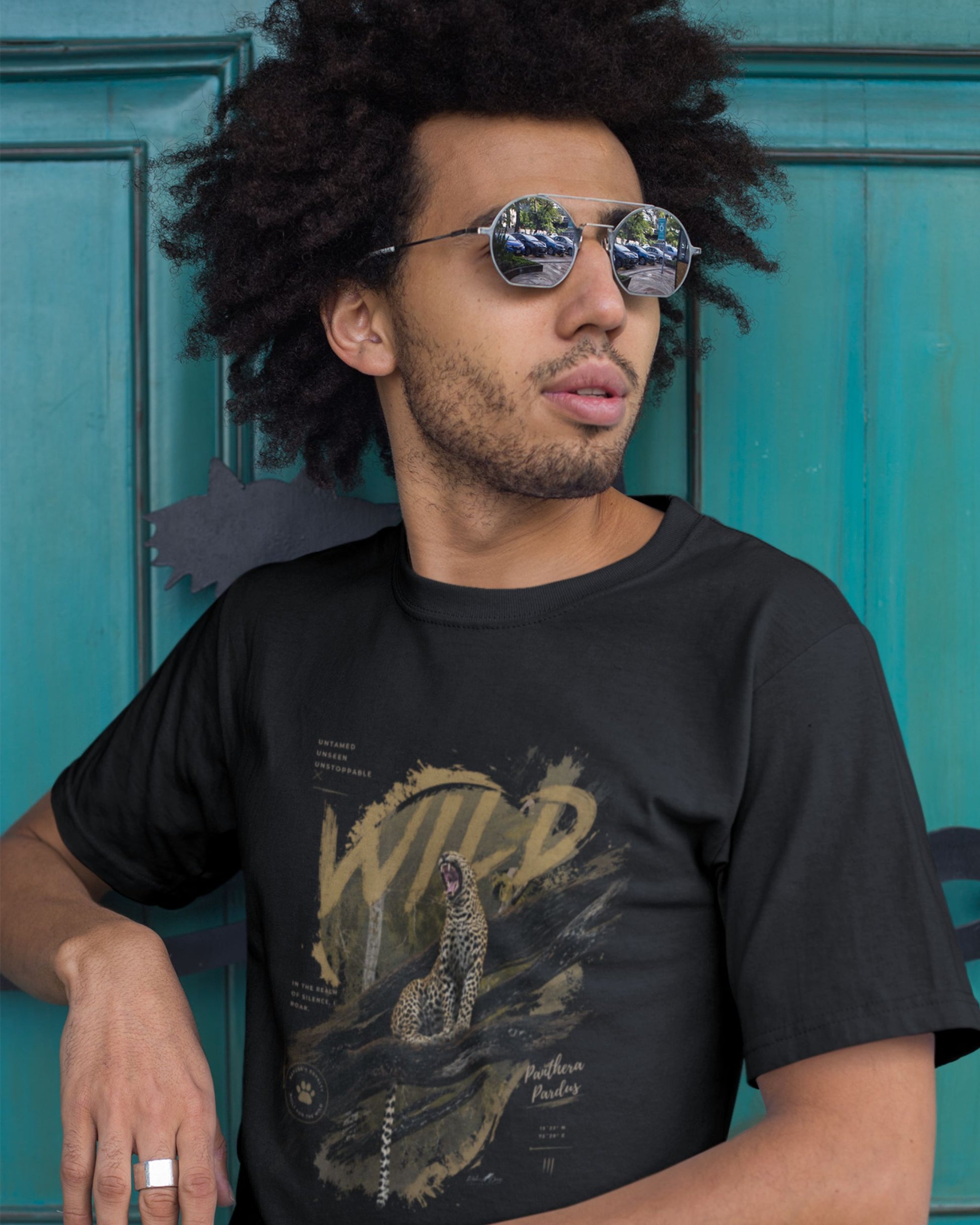 Man wearing a black tucktribe t-shirt with a leopard graphic design in front of a blue door.