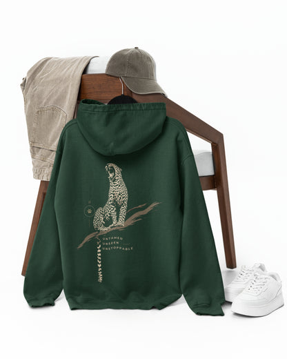 A dark forest green hoodie with a detailed leopard graphic on the back, styled on a wooden chair with a beige shirt, a gray cap, and white sneakers on a white background.