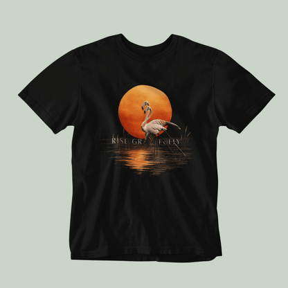 A black Tucktribe short-sleeve crewneck t-shirt featuring a graphic print of a pink flamingo standing in front of a large orange sun over water, with the text 'RISE GRACEFULLY' printed below the sun.