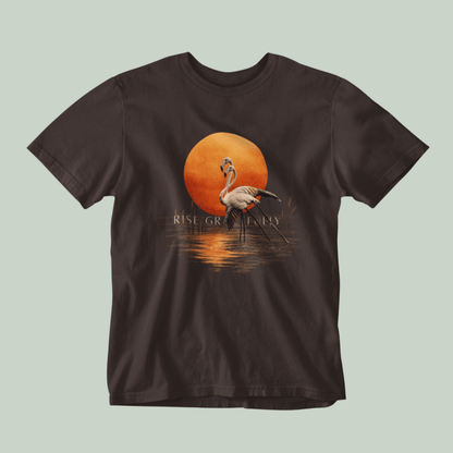 A brown Tucktribe short-sleeve crewneck t-shirt featuring a graphic print of a pink flamingo standing in front of a large orange sun over water, with the text 'RISE GRACEFULLY' printed below the sun.