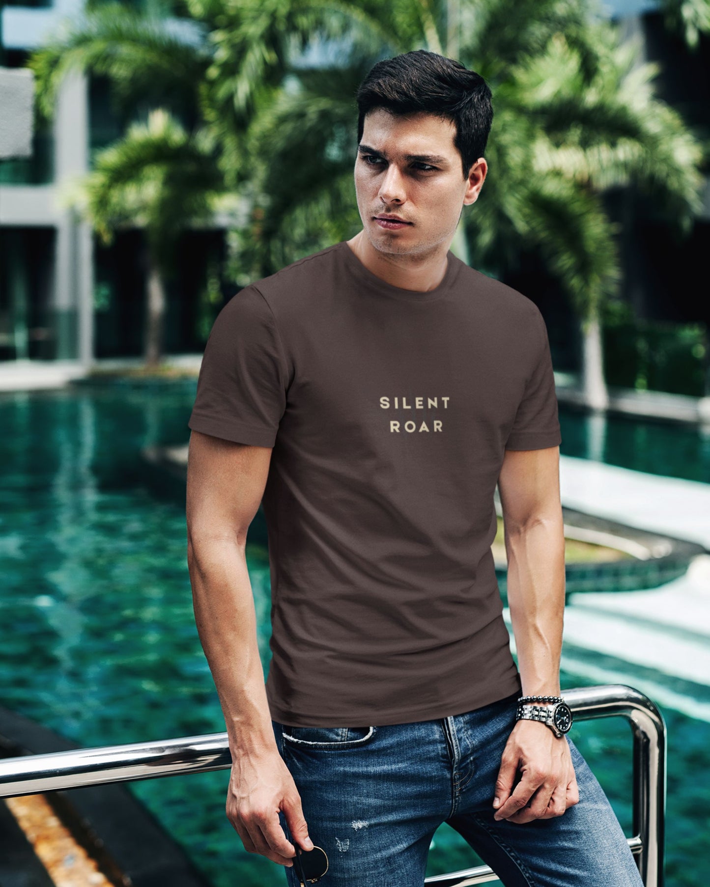 Man wearing a brown Tucktribe t-shirt with 'SILENT ROAR' text by a poolside.