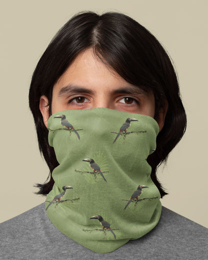 Person wearing a green tucktribe neck gaiter with collared aracari bird pattern against a beige background